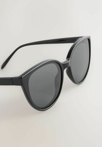 Lunettes de soleil noires style œil de chat avec verres teintés foncés reposant sur une surface claire.