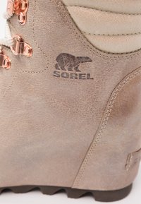 Stivale in pelle marrone con superficie texturizzata, dotato di accessori in oro rosa e logo Sorel. Progettato per la durata con una suola robusta.