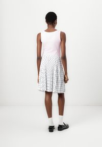 Un débardeur rose clair associé à une jupe blanche longueur genou avec un motif de grille bleue, agrémenté de chaussures noires et de chaussettes blanches.