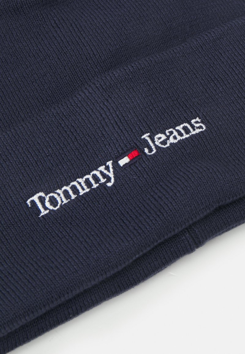 Navyblaues Strickmütze mit weißem und rotem gesticktem "Tommy Jeans"-Logo. Ripp-Textur, weicher Stoff und umschlagbares Design.