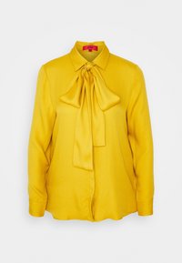 Blouse à manches longues jaune moutarde avec col pointu et grand nœud noué au niveau de l'encolure, en tissu lisse.