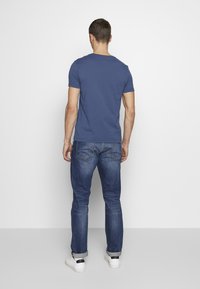 T-shirt blu navy a maniche corte abbinato a jeans blu sbiaditi. I jeans sono leggermente arrotolati ai polsini, indossati con sneakers bianche.