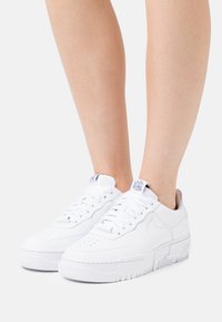 Sneaker bianche in pelle con una texture liscia, punta rotonda e suola in gomma spessa con battistrada a motivo e un marchio discreto sul tallone.