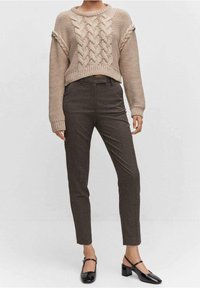 Pull en tricot beige avec motif torsadé, coupe courte. Pantalons marron ajustés, coupe droite. Chaussures noires à talons blocs avec sangle.