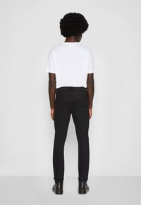 Black denim jeans with a slim fit, mid-rise waist, and a classic five-pocket design. Paired with a white short-sleeve t-shirt.
