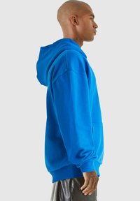 Jasne modré mikina s kapucňou vyrobená z mäkkej tkaniny, s klokaními vreckami, dlhými rukávmi a rebrovanými manžetami a lemom.