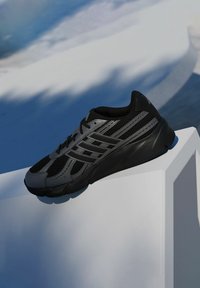 Čierna a sivá športová obuv s sieťovanými panelmi, textúrovanou podrážkou a šiestimi dierkami na šnúrky, umiestnená na bielej geometrickej ploche.