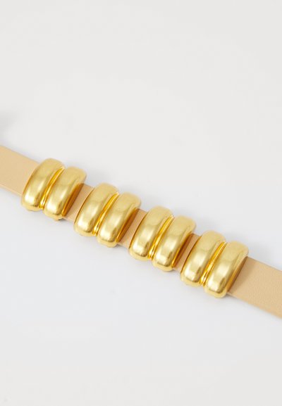Cintura in pelle beige con sei eleganti dettagli in metallo dorato disposti uniformemente lungo la cinghia, creando un design audace e contemporaneo.
