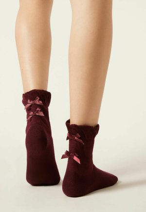Chaussettes jusqu'à la cheville bordeaux avec des volants et deux petits nœuds en satin à l'arrière. Texture douce et design ajusté.