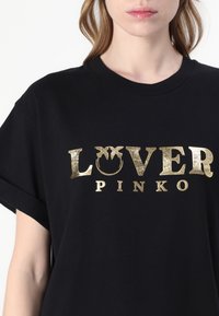 Juoda marškinėliai su auksinės spalvos metaliniu užrašu "LOVER PINKO." Trumpomis rankovėmis ir apvaliu iškirpimu. Minkšta audinio tekstūra.