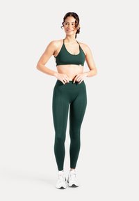 Set sportivo verde scuro composto da reggiseno e leggings in tessuto elastico, con collo all'americana e design senza cuciture. Indossato con sneakers bianche.