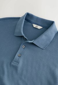 Polo shirt azzurro chiaro con un design a maglia testurizzata, dotato di colletto a costine, placca con tre bottoni e vestibilità standard.