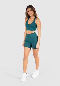 Teal sportoutfit met een geribbelde crop top en high-waisted shorts. Gemaakt van rekbaar materiaal. Witte sneakers met zichtbare merkbenaming.