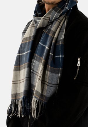 Wollen sjaal in marineblauw, grijs en crème met een ruitpatroon. Heeft franjes aan de randen en een zachte textuur die om de nek hangt.