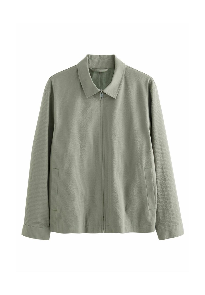 Veste zippée vert clair avec col et manches longues, dotée de deux poches latérales et d’un tissu subtilement texturé.