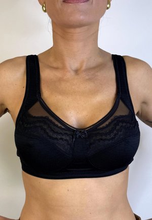 Sosten negro con tejido texturizado, paneles de malla transparente, bordes de encaje y un pequeño lazo en el centro delantero. Con tirantes ajustables.