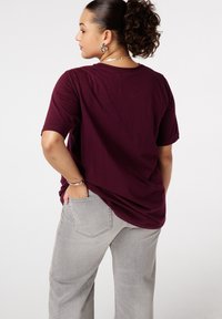 Bordeaux T-shirt met korte mouwen en een relaxte pasvorm, gecombineerd met lichtgrijze wijde broek met achterzakken en een vervaagde textuur.