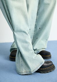 Light blue wide-leg denim jeans with prominent stitching, paired with chunky black platform shoes featuring yellow accents.