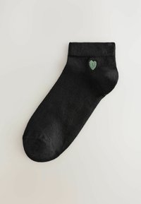 Crna čarapa do gležnja izrađena od glatkog materijala, s malim vezom zelene srca blizu pete. Jednostavan dizajn s rebrastim rubom.