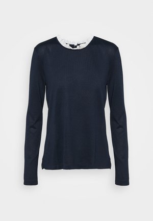 Haut à manches longues bleu marine avec détail de col à volants en dentelle blanche et fermeture par bouton à œillet dans le dos.