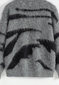 Pull gris à texture duveteuse avec des formes géométriques abstraites noires et des lignes sur la poitrine et les manches.