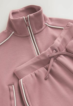 Sweatshirt zippé rose clair avec un col haut et des accents blancs, associé à un pantalon de survêtement assorti avec une taille élastique et un cordon de serrage.