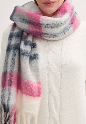 Soft wool scarf featuring a plaid pattern with pink, gray, and navy shades, fringed ends, draped over a cream-colored knit sweater.