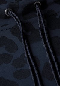 Tessuto blu navy con un delicato motivo a macchie di leopardo, dotato di due corde scure e occhielli in metallo neri per la regolazione. Texture morbida.