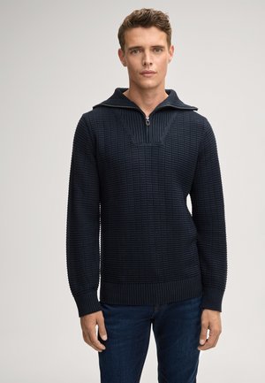 Sweter w kolorze granatowym, z zamkiem przy kołnierzu, teksturowanym wzorem oraz ściągaczami przy mankietach i u dołu. Dopasowany fason z V-kształtnym detalem na klatce piersiowej.