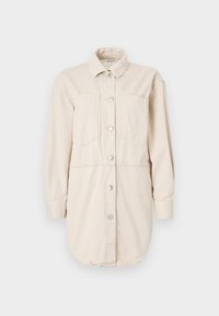 Beige shirt dress made of cotton with long sleeves, button closure, two chest pockets, and a slightly curved bottom hem.