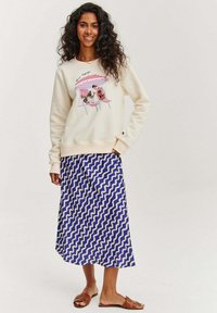 Krémová mikina s grafickým potiskem psů na plážových křeslech. Modrá maxisukně se bílými vlnkovanými liniemi. Hnědé sandály na klínku.