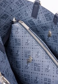 Sac à main à motif bleu avec un intérieur texturé, une fermeture éclair argentée et un logo. Matériau en nylon avec motifs géométriques et équestres.
