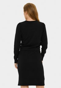 Robe noire à manches longues avec une silhouette ajustée, des poignets et une taille côtelés ; simple encolure ronde avec une texture subtile.
