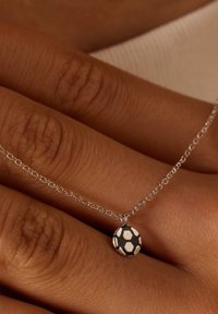Zilveren ketting met een kleine hanger in de vorm van een voetbal, met zwart-witte hexagonale patronen, rustend op een hand.