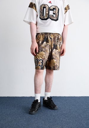 Maillot blanc avec le numéro noir "03" et un short camouflage aux motifs sombres. Baskets noires avec des accents, accompagnées de chaussettes blanches.