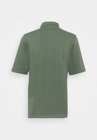 Polo à manches courtes en vert olive, en coton, doté d’un col classique et de coutures nettes le long de l’ourlet et des manches.