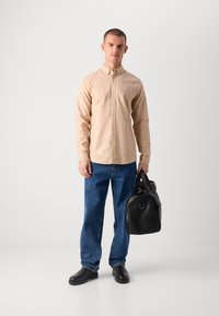 Chemise beige à boutons, jean bleu, chaussures noires en cuir lisse, et un sac noir texturé avec une poignée. Design simple et ajusté sans motifs visibles.
