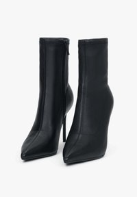 Zwarte enkellaarsjes met hoge hak, gemaakt van glad leer. Voorzien van een puntige neus, ritssluiting en een strak, aangesloten ontwerp.