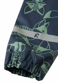 Tessuto impermeabile blu navy con un motivo animale astratto verde. Polsino elasticizzato con una fascia riflettente grigia e dettagli con logo.