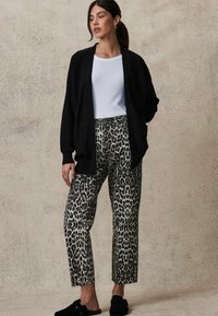 Svart ruggad cardigan och vit åtsittande t-shirt i kombination med mönstrade grå och svarta leopardmönstrade byxor. Svart slip-on skor.