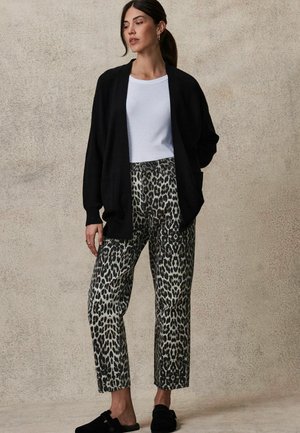 Sort ribbet cardigan og hvid tætsiddende t-shirt parret med mønstrede grå og sorte leopardprint bukser. Sorte slip-on sko.