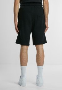 Svarta ribbade shorts med elastisk midja och en bakficka, tillsammans med vita strumpor och sneakers, vy från baksidan.