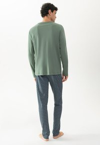 Groene lange mouwen shirt met ronde hals, gecombineerd met marineblauwe gestreepte broek met kleine witte geometrische vormen.