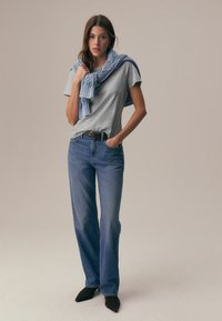 Siva majica s kratkimi rokavi, modre kavbojke in modra pletena ruta, ki je premetena čez ramena. Črne čevlje z ozkim sprednjim delom.