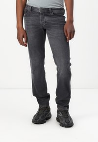 Jeans de mezclilla gris oscuro con corte recto, diseño de cinco bolsillos, sutil desgaste y costuras en contraste. Combinados con zapatillas negras.