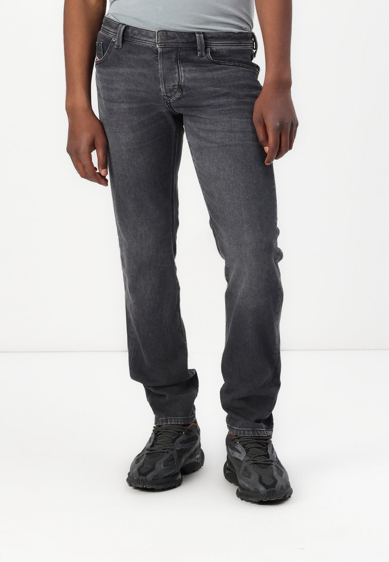 Jeans de mezclilla gris oscuro con corte recto, diseño de cinco bolsillos, sutil desgaste y costuras en contraste. Combinados con zapatillas negras.