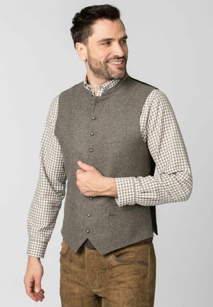 Braune Wollweste mit hohem Kragen, vorderen Knöpfen und Seitentaschen, getragen über einem hellbraun-weißen karierten Hemd.