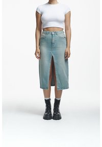 Denim midi skirt in light blue with a front slit; paired with a white cropped t-shirt and black lace-up boots.