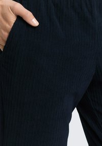 Granatowe, prążkowane spodnie do noszenia w domu o luźnym kroju i bocznej kieszeni; charakteryzują się subtelną fakturą oraz elastycznym paskiem w talii zapewniającym wygodę.