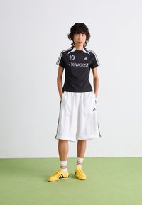 Black short-sleeve jersey with white accents and printed number 10, paired with white shorts. Yellow athletic shoes with black stripes.